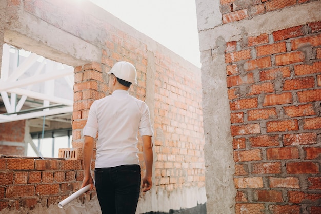 Widok młodego, pewnego siebie architekta z planem zwiniętym w rękę, podczas inspekcji pracy budynku w budowie.