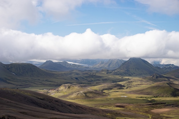 Widok na dolinę górską z zielonymi wzgórzami, strumieniem rzeki i jeziorem. Szlak turystyczny Laugavegur, Islandia.