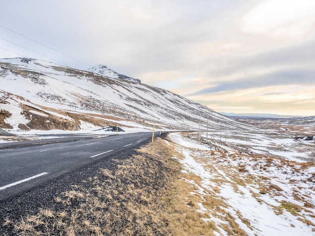 Widok na krajobraz ze śniegiem w sezonie zimowym pod zachmurzonym niebem wzdłuż drogi w Islandii