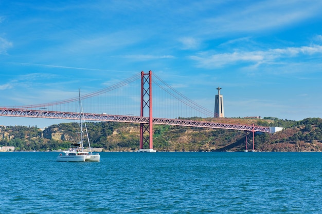 Widok na most de abril nad rzeką tagus pomnik chrystusa króla i jacht łódź lizbona portugalia