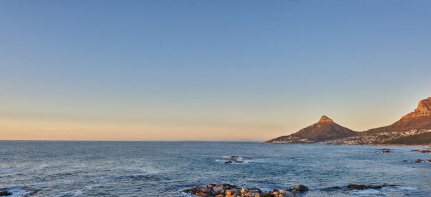 Widok na ocean wody morskiej na skalistych plażach gór i błękitne niebo z kopią głowy lwa w Cape Town w RPA Spokojny przypływ pogodna i spokojna sceneria relaksującej matki natury o wschodzie słońca