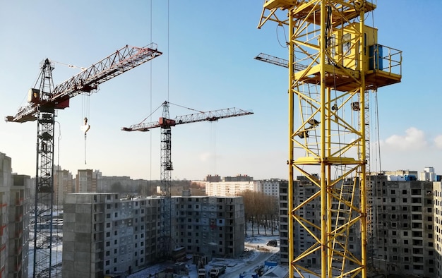 Widok na plac budowy w zimowy słoneczny mroźny dzień. Budowa budynków mieszkalnych z wykorzystaniem żurawi wieżowych.