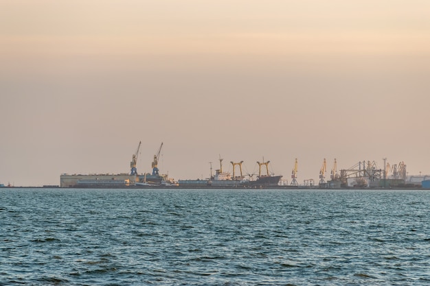 Widok na port morski z dźwigami i statkami podczas zachodu słońca.