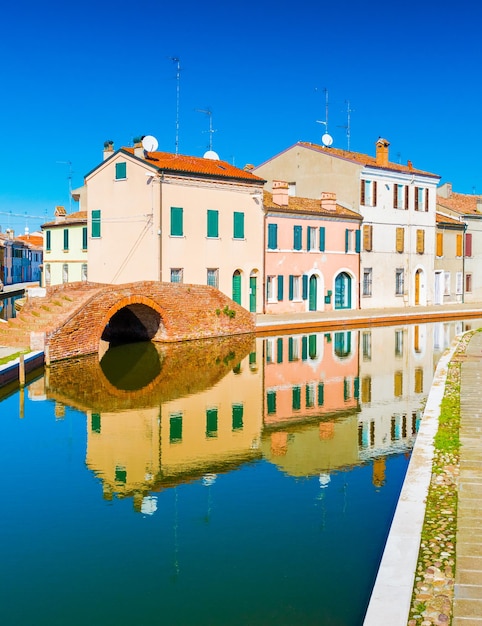 Widok na stare włoskie miasto z kolorowymi domami odbitymi w wodzie. Małe włoskie miasteczko Comacchio, prowincja Ferrara. Pusta ulica z kanałem bez łodzi i stare domy mieszkalne