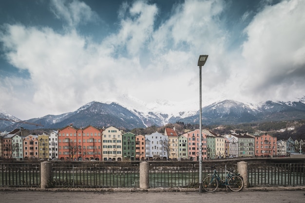 Widok na zabytkowe centrum Innsbrucku z kolorowymi domami wzdłuż rzeki Inn i słynnymi górskimi szczytami Austrii w tle z rowerem, Tyrol, Austria