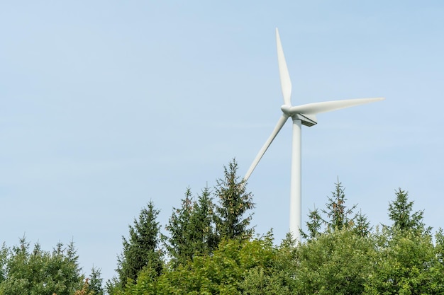 Widok nowoczesnego wiatraka na tle błękitnego nieba Białe łopaty turbiny wiatrowej Turbiny wiatrowe w lesie z dala od wielkiego miasta w letni dzień Czysta i odnawialna produkcja energii