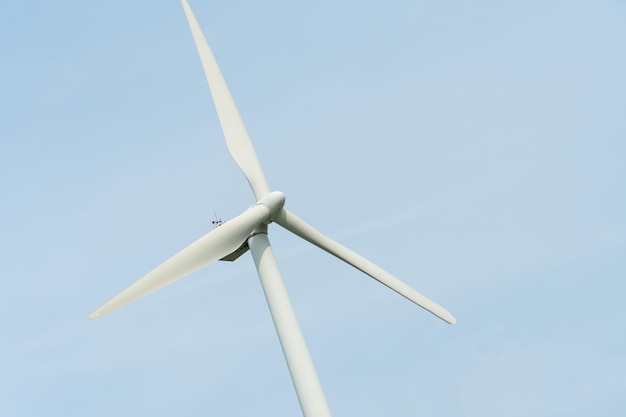 Widok nowoczesnego wiatraka na tle błękitnego nieba Białe łopaty turbiny wiatrowej Turbiny wiatrowe w lesie z dala od wielkiego miasta w letni dzień Czysta i odnawialna produkcja energii