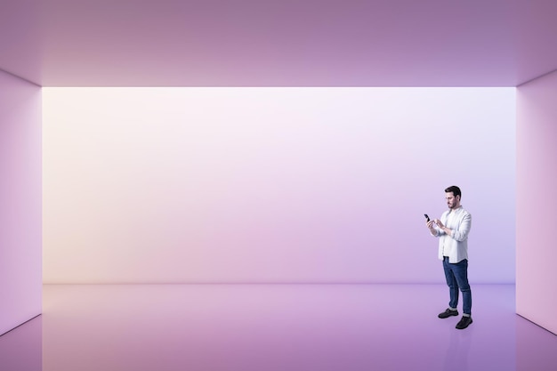 Widok perspektywiczny na młodego mężczyznę używającego smartfona w pustym przestronnym obszarze z fioletowymi cieniami tła ściany przestrzeni dla makiety prezentacji produktu lub samochodu