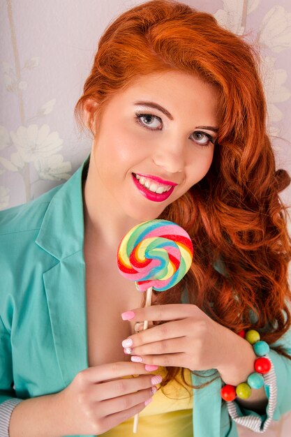 Widok piękna rudzielec dziewczyna jest ubranym kolorową odzież z lollipop cukierkiem.