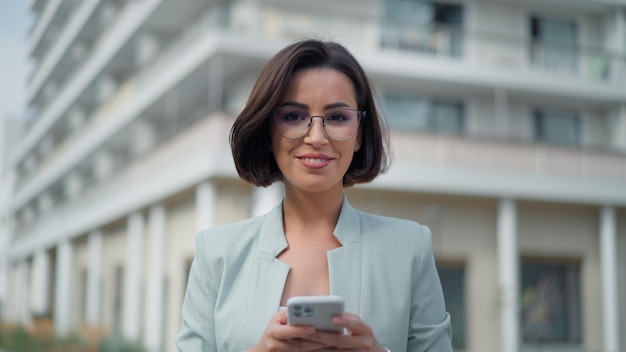 Widok portretowy szczęśliwej kobiety patrzącej na ekran telefonu komórkowego podczas rozmowy online na ulicy miasta