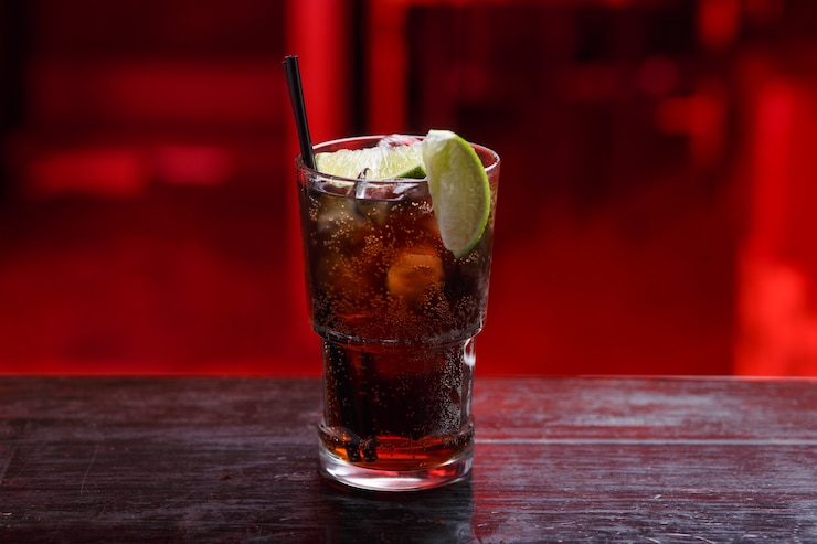 Zdjęcie widok poziomy. zbliżenie na koktajl cuba libre w długiej szklance, gin, stojąc na ladzie barowej, odizolowane na czerwonej przestrzeni.