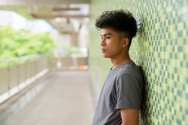 Widok profilu młodego mężczyzny z Azji z kręconymi włosami przy kładce dla pieszych w mieście