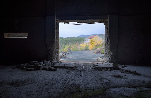 Widok przez drzwi opuszczonej fabryki na tle jesieni