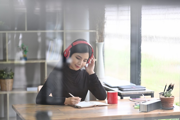 Widok przez okno ładnej kobiety projektanta słuchania muzyki i pracy w nowoczesnym biurze.