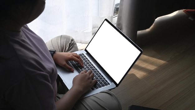 Widok przez ramię otyłej kobiety korzystającej z laptopa i siedzącej na podłodze w salonie