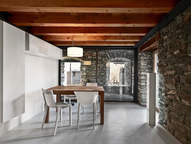 Widok wnętrza jadalni z plastikowymi krzesłami i drewnianym stołem oraz sufit, ściany z kamienia, podłoga z betonu