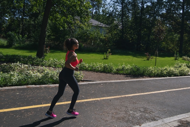Widok z boku biegacza kobieta joggingu na drodze w parku. Fitness na świeżym powietrzu