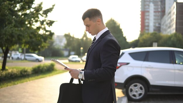 Widok z boku biznesmena patrzącego na dokumenty czekające na spotkanie na świeżym powietrzu w pobliżu centrum biznesowego w słoneczny dzień