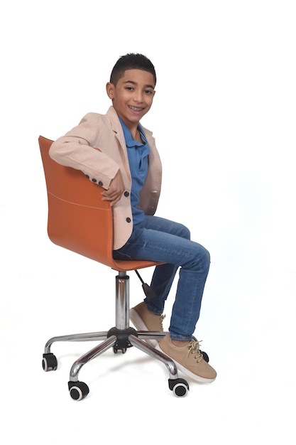 Widok z boku chłopca siedzącego na krześle odwróconym i patrzącego w kamerę na białym tle