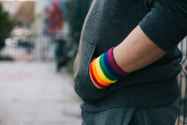 Widok z boku chłopca z bransoletą dumy gejowskiej z rękami w kieszeni stoi na ulicy