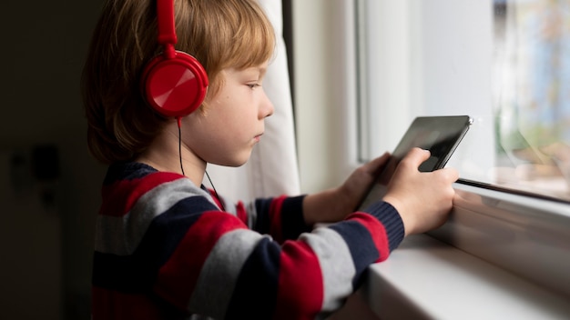 Zdjęcie widok z boku chłopca za pomocą tabletu ze słuchawkami