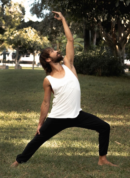 Zdjęcie widok z boku człowieka robi joga na trawie na zewnątrz