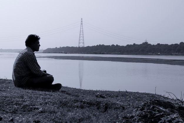Zdjęcie widok z boku człowieka siedzącego na moście nad rzeką na tle nieba