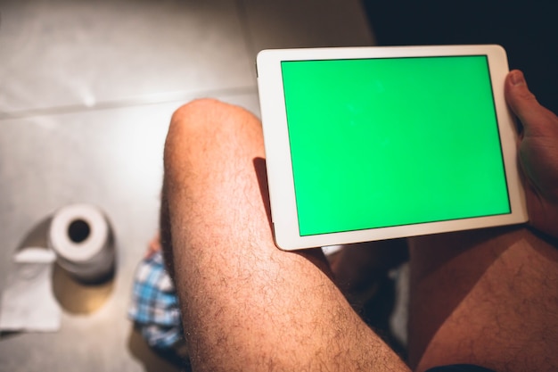 Widok Z Boku Człowieka Z Owłosionymi Nogami Siedzącego Na Garnku W Pokoju Wypoczynkowym I Trzymaj Tablet Z Zielonym Ekranem