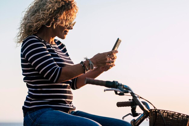 Widok z boku dorosłej kobiety używającej połączenia telefonu komórkowego do przesyłania wiadomości siedzącej na klasycznym rowerze Zielony transport środowiskowy styl życia Kobiety lubią wypoczynek na świeżym powietrzu i połączenie z internetem