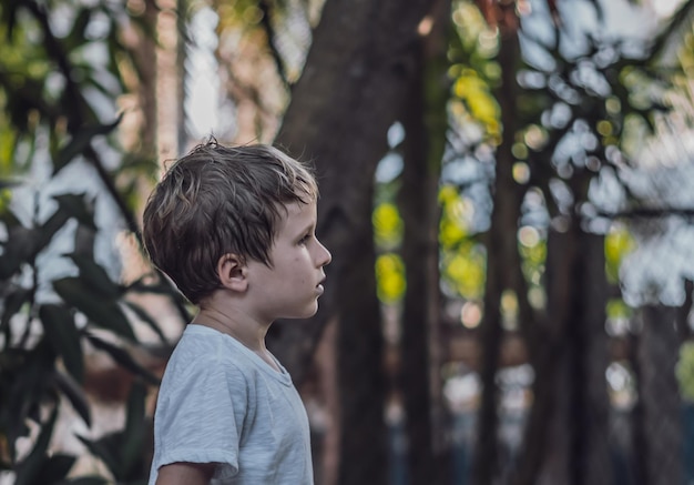 Widok z boku dziecko dziecko sześcioletni chłopiec patrzący prosto poważny smutny w białej koszulce na zewnątrz przyrody Ciemny nastrój dzieciństwo rodzicielstwo psychologia edukacja problemy kryzys ze względu na koncepcję COVID