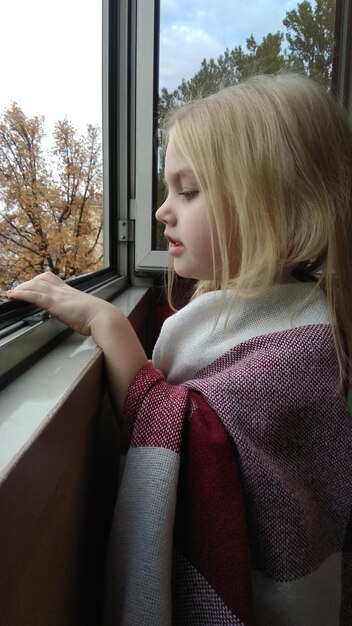 Zdjęcie widok z boku dziewczyny patrzącej przez okno w domu