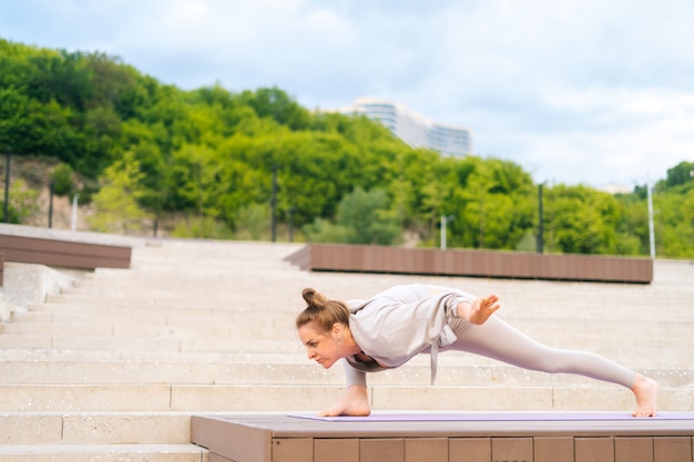 Widok z boku elastycznej młodej joginki ćwiczącej ćwiczących jogę na macie fit w letni dzień