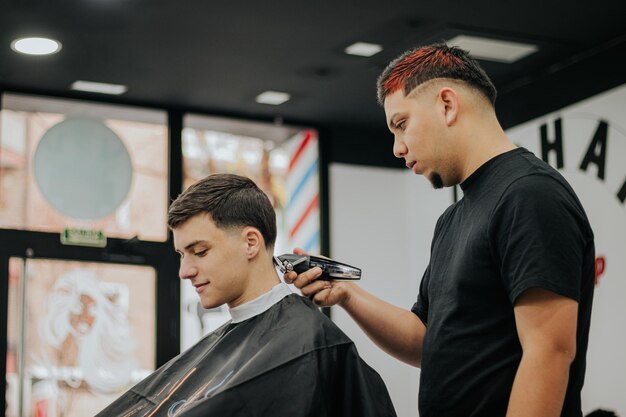 Zdjęcie widok z boku fryzjera i klienta podczas strzyżenia włosów klienta w jego salonie