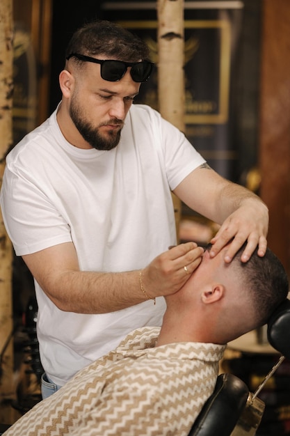 Zdjęcie widok z boku fryzjera przycinającego brwi pęsetą dla pewnego siebie mężczyzny