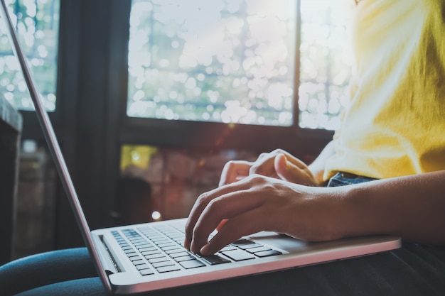 Widok z boku i powiĘ urocza młoda dziewczyna hipster dziewczyna pracy na swoim laptopie siedzi na drewnianym stole w kawiarni. kobieta przy użyciu komputerów w kawiarni - vintage kolorowy styl.