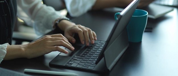 Widok z boku kobiecych rąk, wpisując na klawiaturze cyfrowego tabletu na stole konferencyjnym