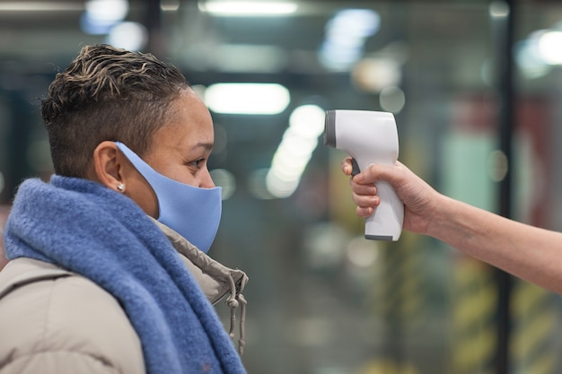 Zdjęcie widok z boku kobiety w masce ochronnej sprawdzającej jej temperaturę przed wejściem do supermarketu