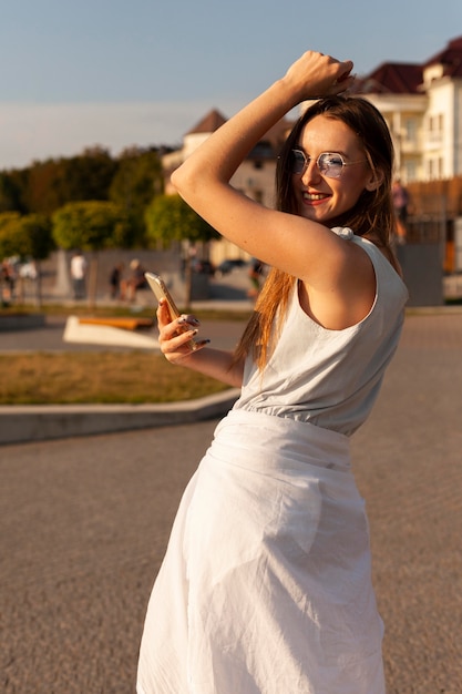 Zdjęcie widok z boku kobiety z okulary i smartfon pozowanie na zewnątrz