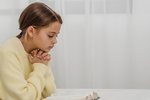Widok z boku małej dziewczynki modlącej się w domu z miejsca na kopię