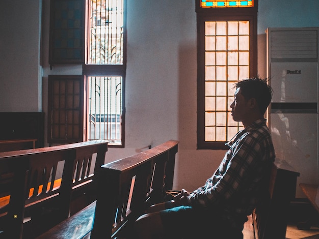Widok z boku mężczyzny modlącego się siedzącego na stole w kościele