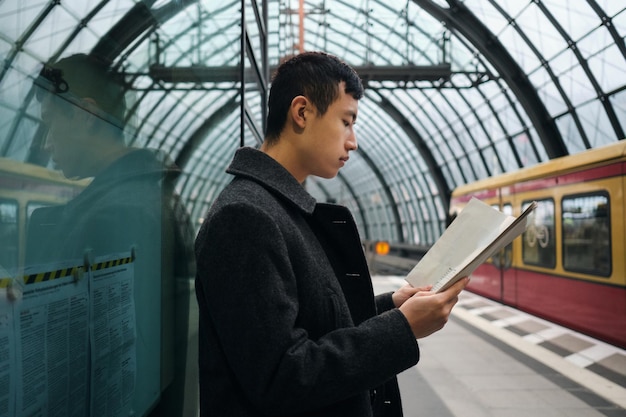 Widok z boku młodego azjatyckiego biznesmena uważnie czytającego gazetę podczas oczekiwania na pociąg na stacji metra