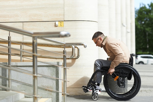 Widok z boku młodego mężczyzny siedzącego na wózku inwalidzkim za pomocą rampy do poruszania się po budynku
