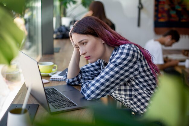 Widok z boku młodej bizneswoman siedzącej przy stole w kawiarni na stole filiżanka kawy i laptop...