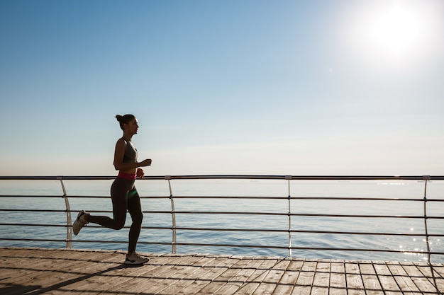 Widok z boku młodej kobiety fitness biegnącej wzdłuż molo.