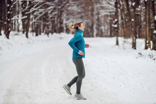 Widok z boku na jogging sportsmenka w lesie w śnieżny, chłodny zimowy dzień. Zimna pogoda, śnieg, zdrowe życie, fitness, las