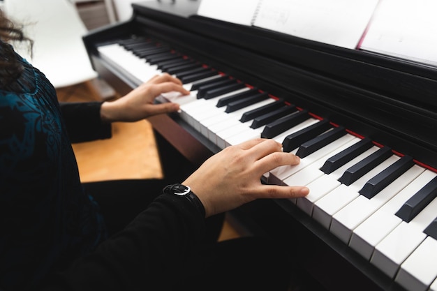 Widok z boku na ręce kobiety, grając na pianinie, czytając nuty. Selektywne skupienie