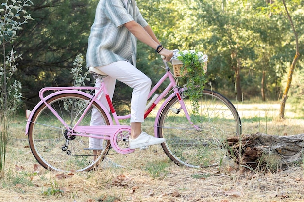 Widok z boku nierozpoznawalnego młodego hipstera na różowym rowerze vintage z naturalnym środowiskiem