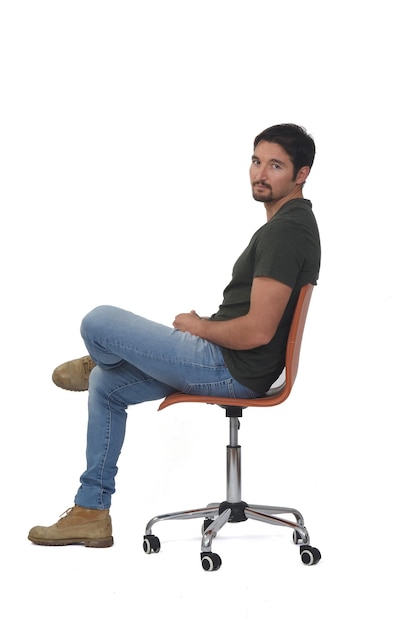 Widok z boku pełnego portretu mężczyzny siedzącego na krześle, patrzącego na kamerę i skrzyżowanych nóg na tle whige