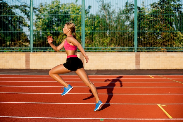 Zdjęcie widok z boku piękna młoda kobieta ćwiczy jogging i bieganie na torze lekkoatletycznym na stadionie