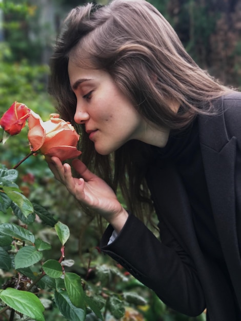 Zdjęcie widok z boku pięknej kobiety pachnącej różą w parku